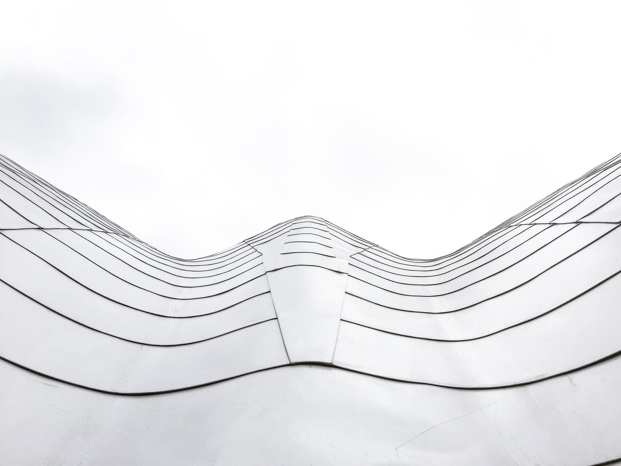 A white metal facade folding in waves against a pale sky